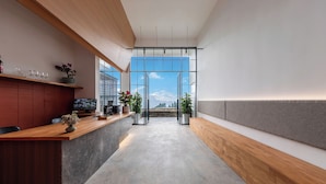 Una zona de recepción moderna con un mostrador de madera, plantas en macetas y vistas amplias a través de puertas de cristal.