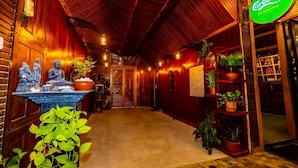 A hallway with wooden walls, a ceiling with wooden beams, and a sign for Carlsberg Denmark. There are potted plants along the walls and a table with statues and a bowl. - Cinnamon Airport Residences (seeduwa)