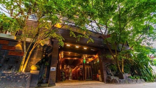 A building entrance with a covered walkway, stone walls, and potted plants. - Cinnamon Airport Residences (seeduwa)