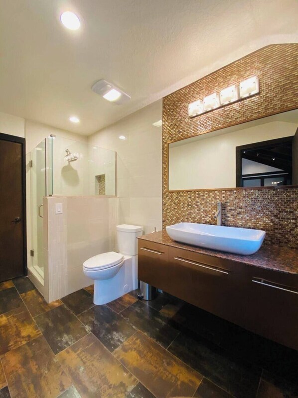 A modern bathroom with a glass shower enclosure, a white toilet, and a large rectangular sink with a mosaic backsplash. - Snowshoe Condo (Brian Head)