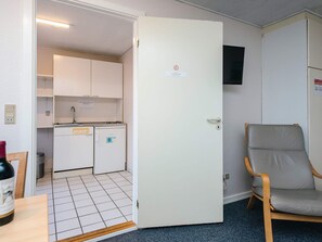A room with a kitchenette, a door with a sign, a chair, and a television mounted on the wall. - 4 Person Holiday Home in Hojer (Højer)