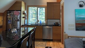 A modern kitchen with wooden cabinets, a stainless steel refrigerator, and a window with a view of trees. - Cabin at Idabel Family, Pet Friendly with Games Room (Kootenay Boundary E / West Bo*)