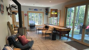 A spacious living area with a fireplace, comfortable seating, and a large window overlooking a deck. - Cabin at Idabel Family, Pet Friendly with Games Room (Kootenay Boundary E / West Bo*)