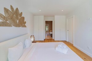 A modern bedroom with a large bed, white walls, and a wooden floor. - Quinta View Apartment (Setúbal)