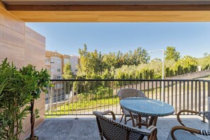 A balcony with a round glass table and wicker chairs, overlooking a residential area with trees and buildings. - Quinta View Apartment (Setúbal)