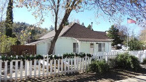 Una casa de una sola planta con cerca blanca en estacas, chimenea y una bandera estadounidense.