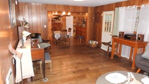 Ein Zimmer mit Holzwandverkleidung, das eine Essecke, ein Wohnbereich mit Sofa und Tisch sowie ein kleiner Tisch mit Lautsprecher umfasst.