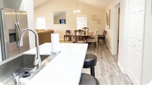 Una cucina moderna con isola centrale, elettrodomestici in acciaio inossidabile e zona pranzo con soffitto alto e illuminazione a sospensione.
