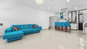 A modern living room with a blue sectional sofa, a kitchen area with bar stools, and a chandelier. - Seaport | Family Home and Shared Pool (Puerto Vallarta)