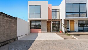 A modern two-story house with a paved courtyard, large windows, and a wooden door. - Seaport | Family Home and Shared Pool (Puerto Vallarta)