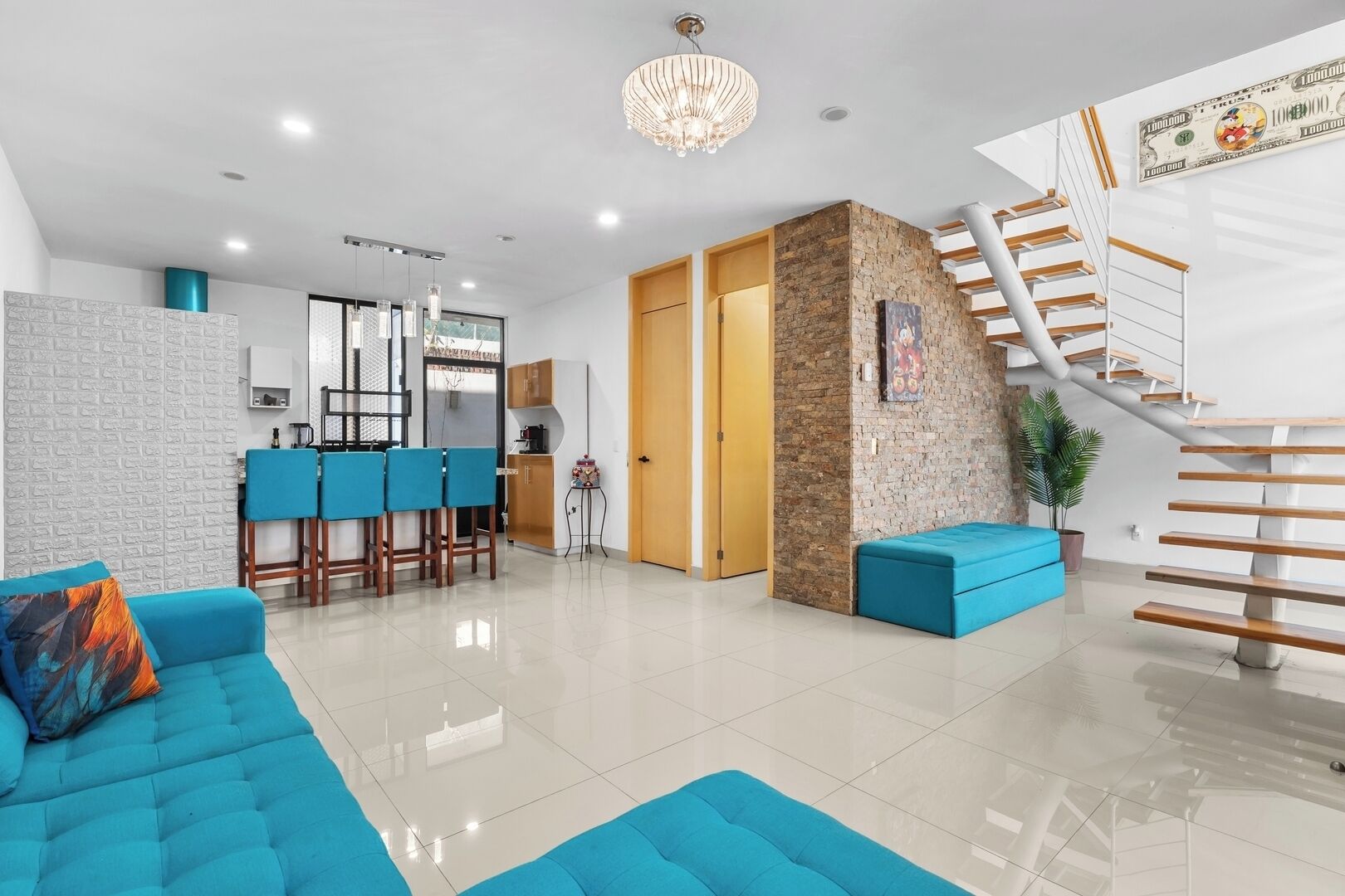 A modern living room with a blue sofa, a kitchen area, and a staircase with a unique design.