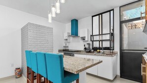 A modern kitchen with white cabinets, a granite countertop, and a blue upholstered chair. - Seaport | Family Home and Shared Pool (Puerto Vallarta)