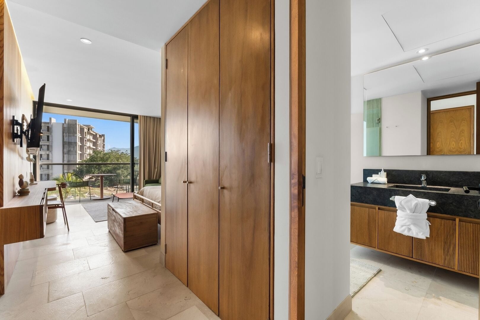Ein modernes Hotelzimmer mit großem Kleiderschrank, einem Balkon mit Stadtblick, einer Küchenzeile inklusive Spüle und einem großen Spiegel über der Arbeitsfläche.