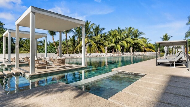 A pool area with lounge chairs and a covered seating area, surrounded by palm trees. - Bright studio at Hotel Mio with pool (Bucerías)
