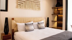 A neatly made bed with a textured headboard, two pillows, and a bedside table with a vase. - Peregrina Tulum 101A 2BR Luxury Condo (Tulum)