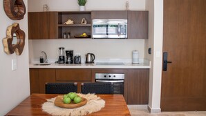 A modern kitchen with wooden cabinets, a stainless steel microwave, and a dining table with a fruit bowl. - Peregrina Tulum 101A 2BR Luxury Condo (Tulum)