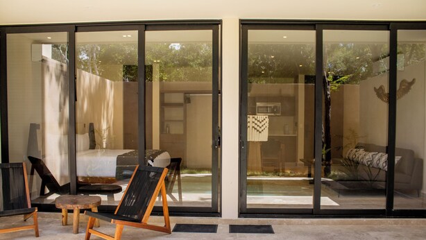 A modern interior with a glass door leading to a balcony, a bed, and a seating area with a table and chairs. - Peregrina Tulum 101A 2BR Luxury Condo (Tulum)