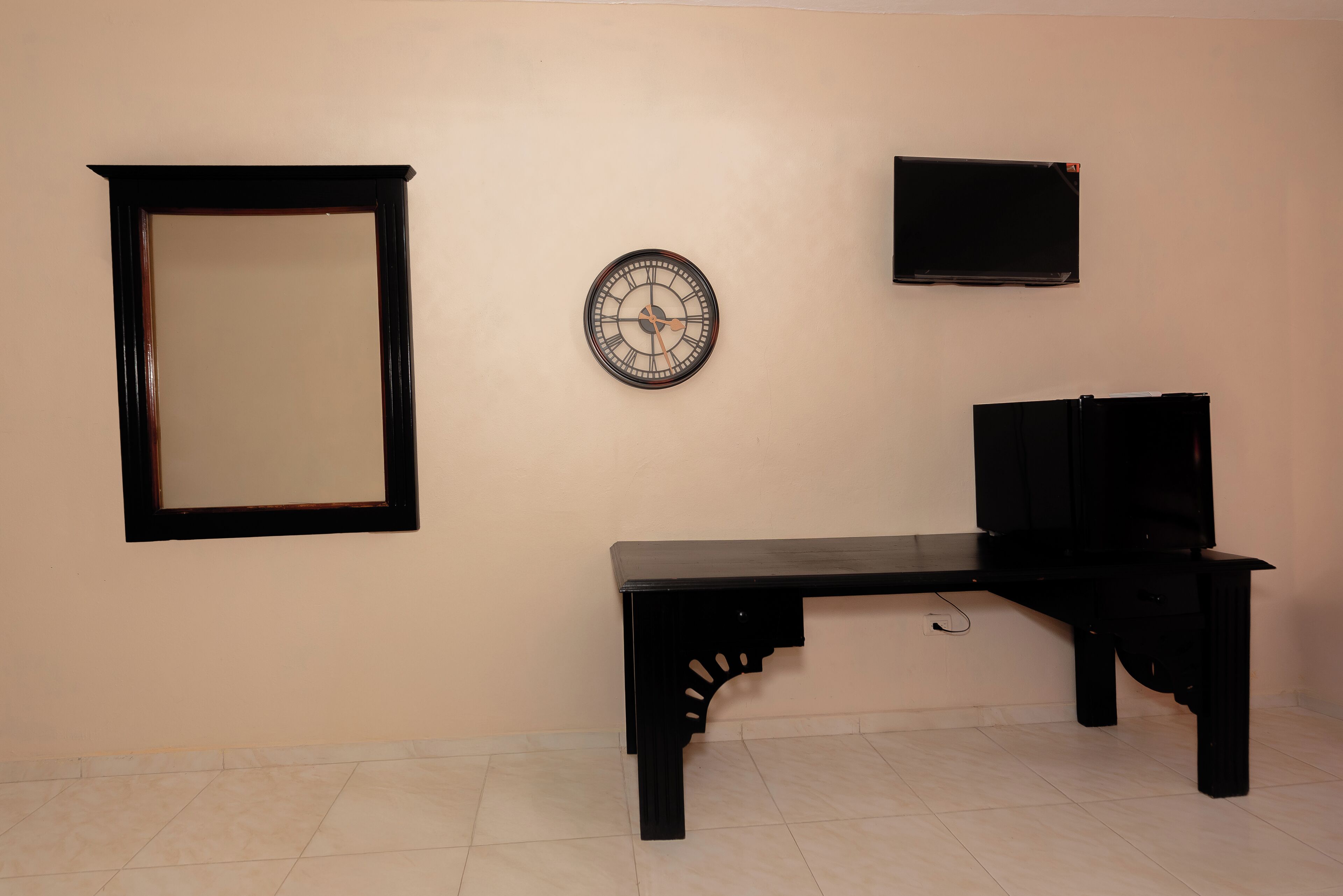 A room with a black desk, a wall-mounted clock, a framed mirror, and a flat-screen TV.