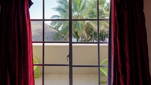 A view through a window with red curtains, revealing a balcony with a tiled floor and two green chairs. - Hotel Boca de Yuma (Boca de Yuma)