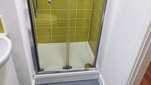 Ducha con puerta de vidrio, paredes de azulejos y un zócalo blanco.