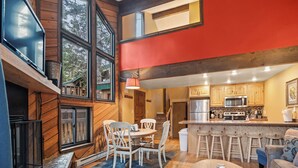 A modern kitchen with wooden cabinets, a central island with stools, and a dining area with a table and chairs. - Ski Access SS7B Retreat Pet Friendly  (Brian Head)