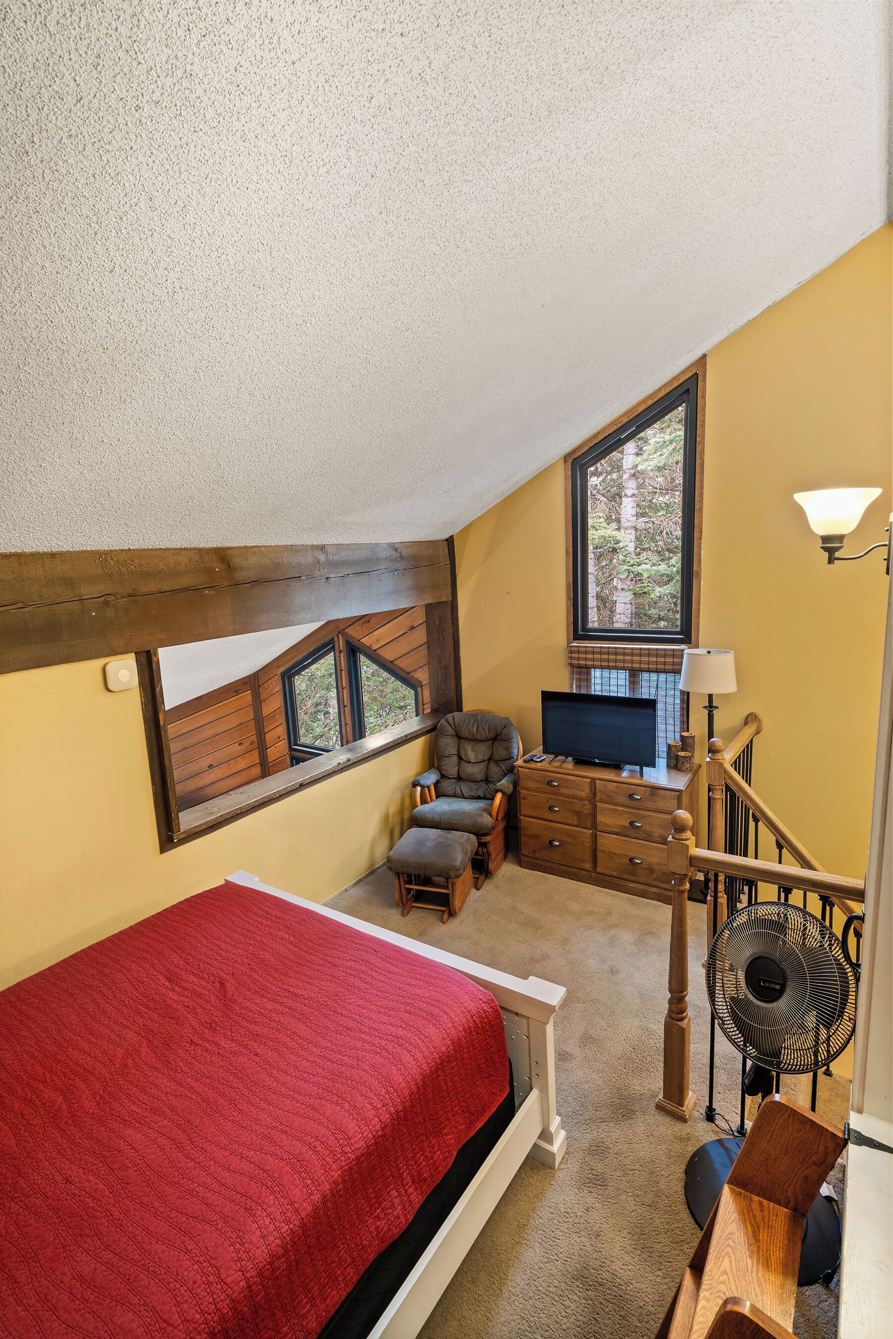 Una camera da letto con una coperta rossa, un comò in legno, una televisione e una finestra vista alberi.