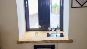 A small window with a wooden ledge, a vase with a flower, and two glassware items.