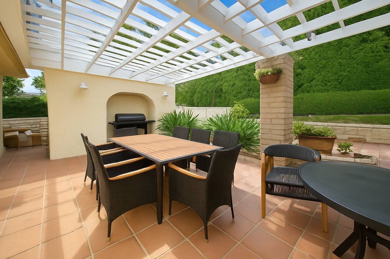 An outdoor patio with a pergola, a grill, and a dining area with chairs and a table.