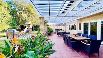 An outdoor patio area with a covered seating area, a play structure, and a dining setup.