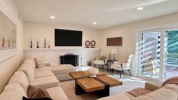 A modern living room with a large sectional sofa, a fireplace, a flat-screen TV, and a dining area with a table and chairs.
