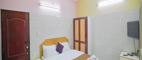 A hotel room with a bed, a desk, a TV, a ceiling fan, and a door.