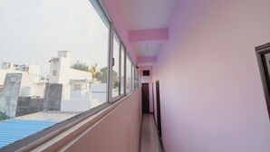 A corridor with pink walls and a window overlooking buildings. - Maruthi Residency (Puducherry)