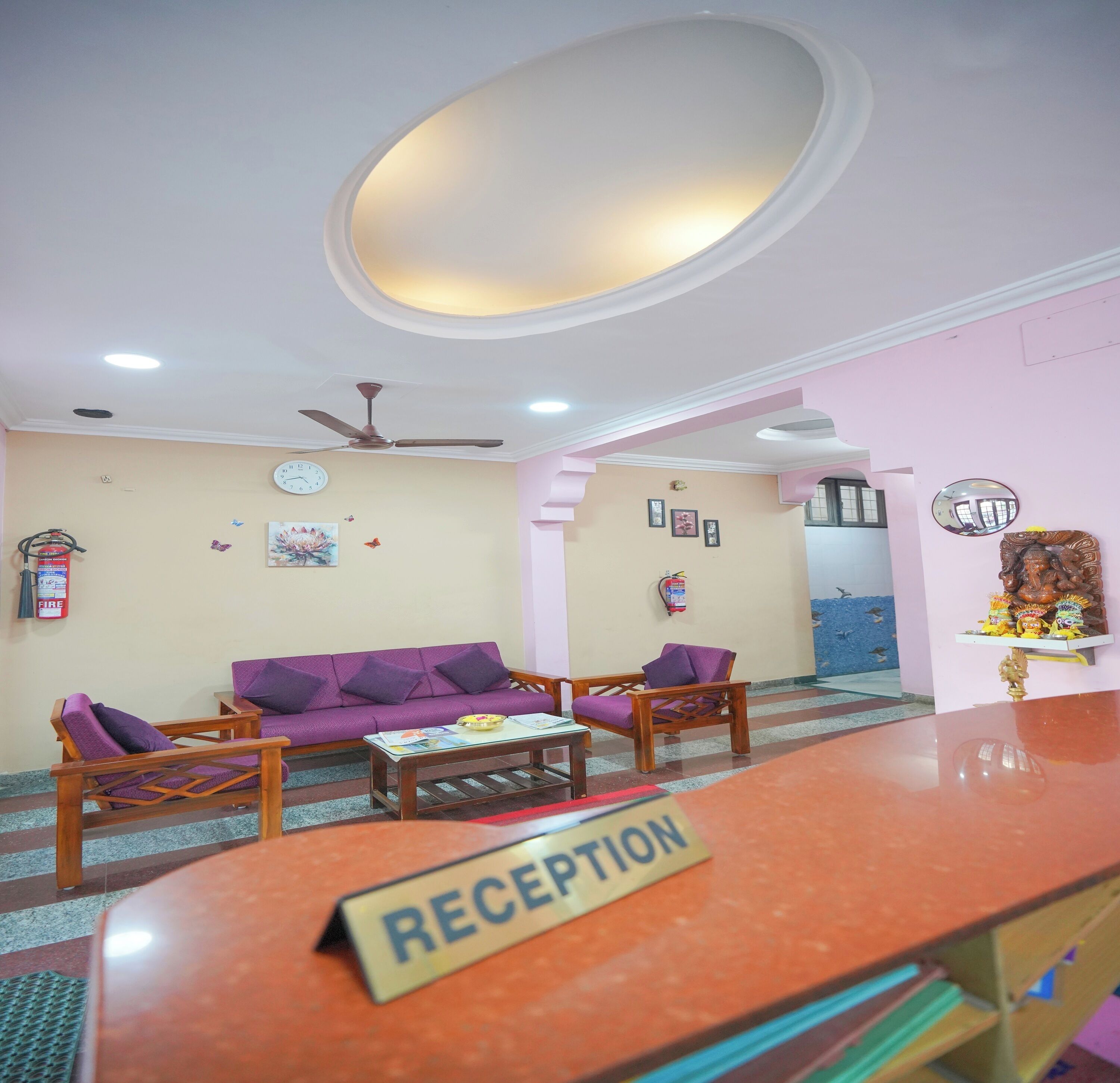 A reception area with a reception desk, purple sofas, a ceiling fan, and a clock on the wall.