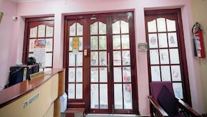 A reception area with a reception desk, two doors with frosted glass panels, ceiling fans, and a fire extinguisher on the wall. - Maruthi Residency (Puducherry)