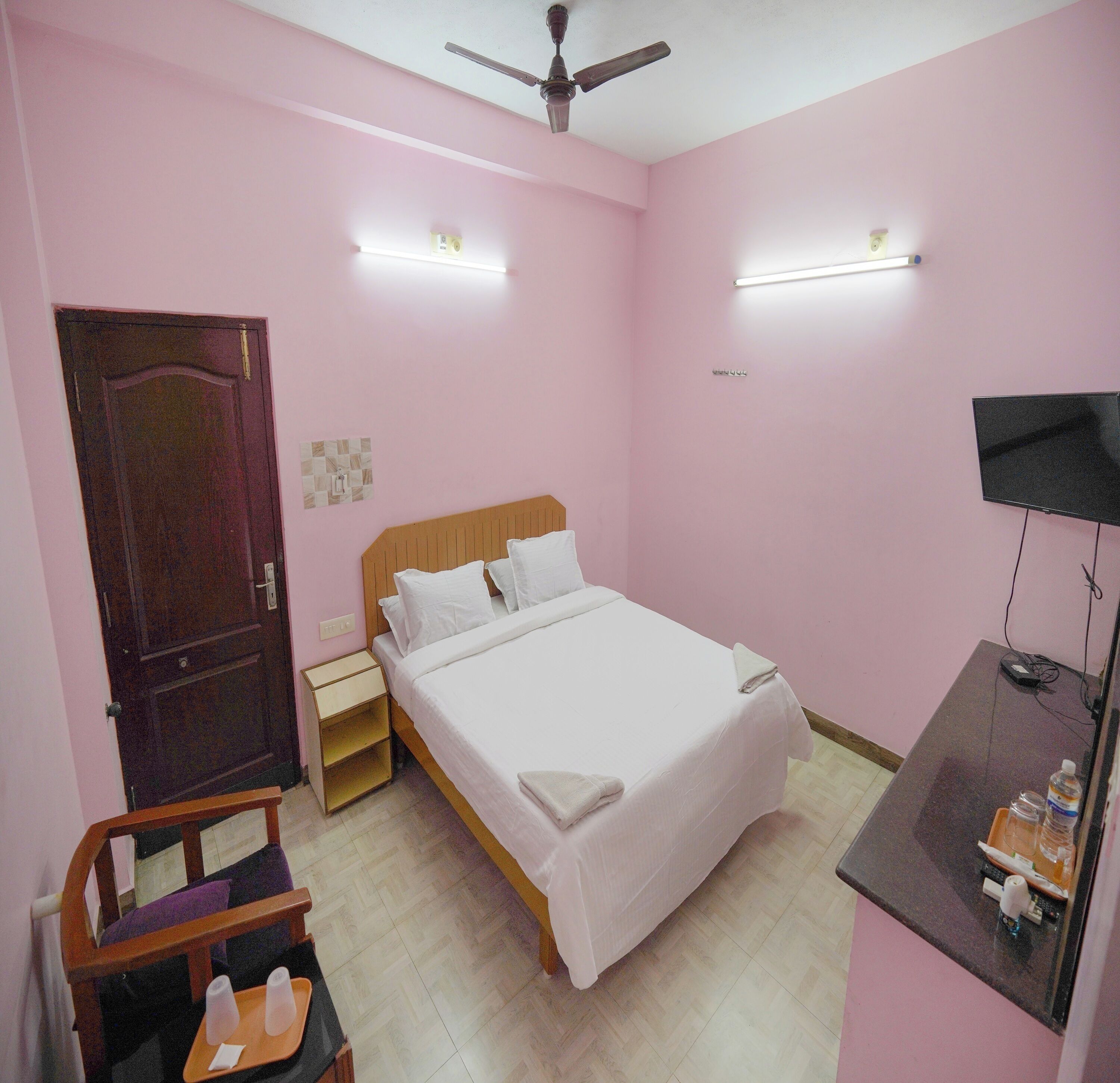 A bedroom with a bed, a wooden nightstand, a desk with a TV, and a ceiling fan.