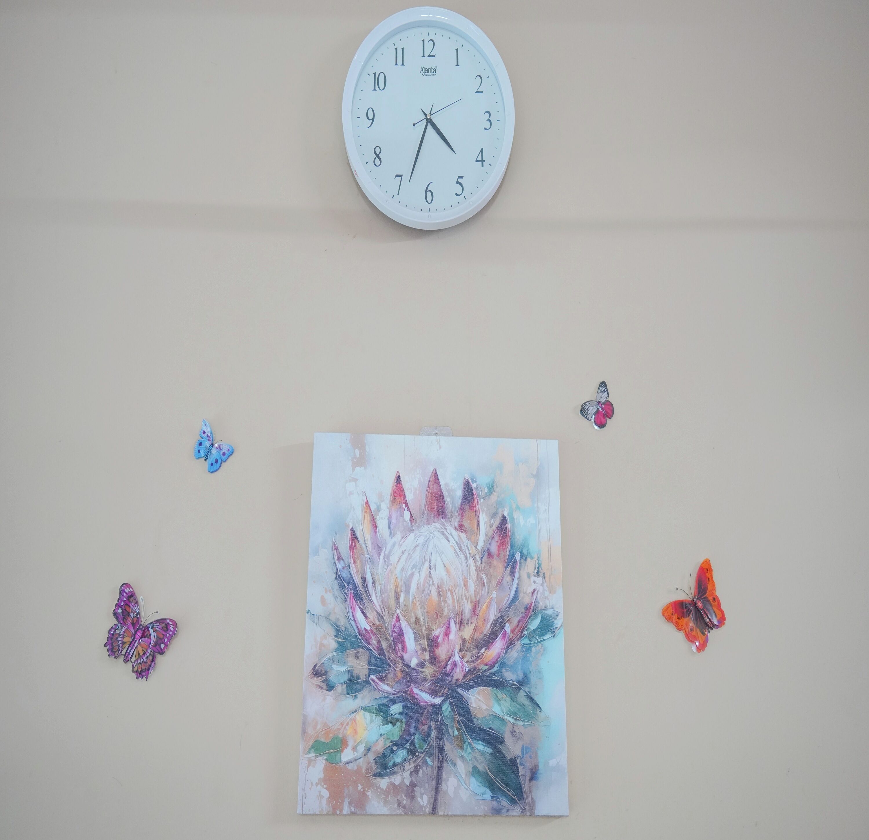 Una pared con un reloj, un cuadro floral y tres adornos de mariposa.
