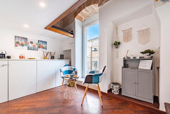 Een moderne keuken met witte kasten, een eethoek met twee stoelen en een uitzicht door een raam.
