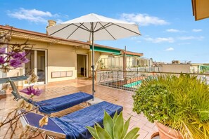 Eine Dachterrasse mit Liegestühlen, einem großen Sonnenschirm und Pflanzen in Töpfen.