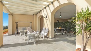 An outdoor patio with white wicker furniture, a swing set, and a potted plant.