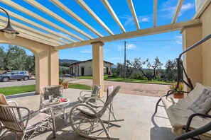 Un espace extérieur aménagé avec des meubles de jardin en osier, notamment des chaises et un canapé, protégé par une pergola et offrant une vue sur une maison et la verdure environnante.