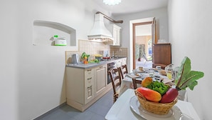 A compact kitchen with a dining area, featuring a central island with a fruit basket, a coffee machine, and a kettle.