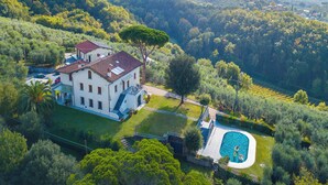A large, white villa with a red roof, surrounded by lush greenery and a swimming pool.