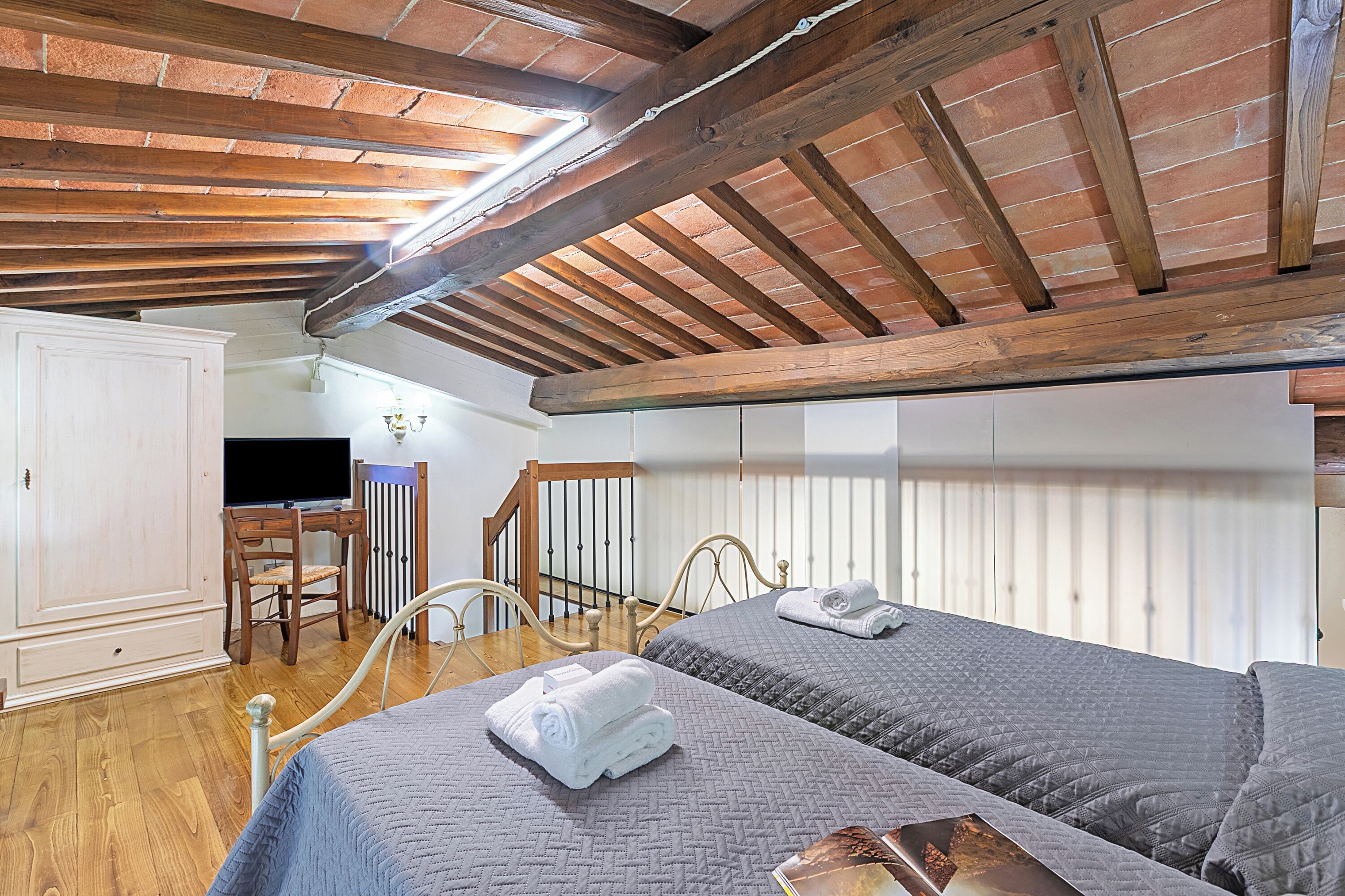 A bedroom with two beds, wooden beams, a television, and a wardrobe.