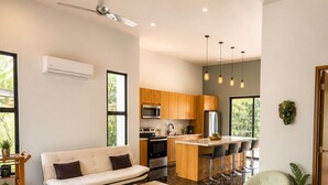 Un salon moderne comprenant un canapé, un coin repas avec des chaises, une cuisine équipée et un ventilateur de plafond.