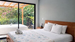 Une chambre à coucher moderne avec un lit en bois, un ventilateur de plafond, une grande fenêtre donnant sur un paysage verdoyant et un sol en marbre.