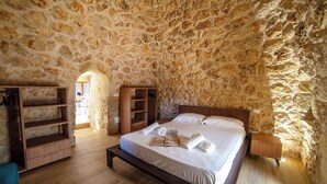 A bedroom with a stone wall, a wooden bed frame, a bedside table, and a built-in wooden shelf. - Trullo Tenuta Mary with Heated Pool, Carpignano Salentino, Italy (Carpignano Salentino)