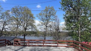 A gravel deck with a wooden fence overlooking a body of water, surrounded by trees. - Lake-Level Retreat w Hot Tub, Picture Windows & 65” TV for Ultimate Relaxation (Monticello)