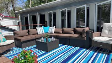A covered outdoor seating area with a sectional sofa, a coffee table, and a striped rug.