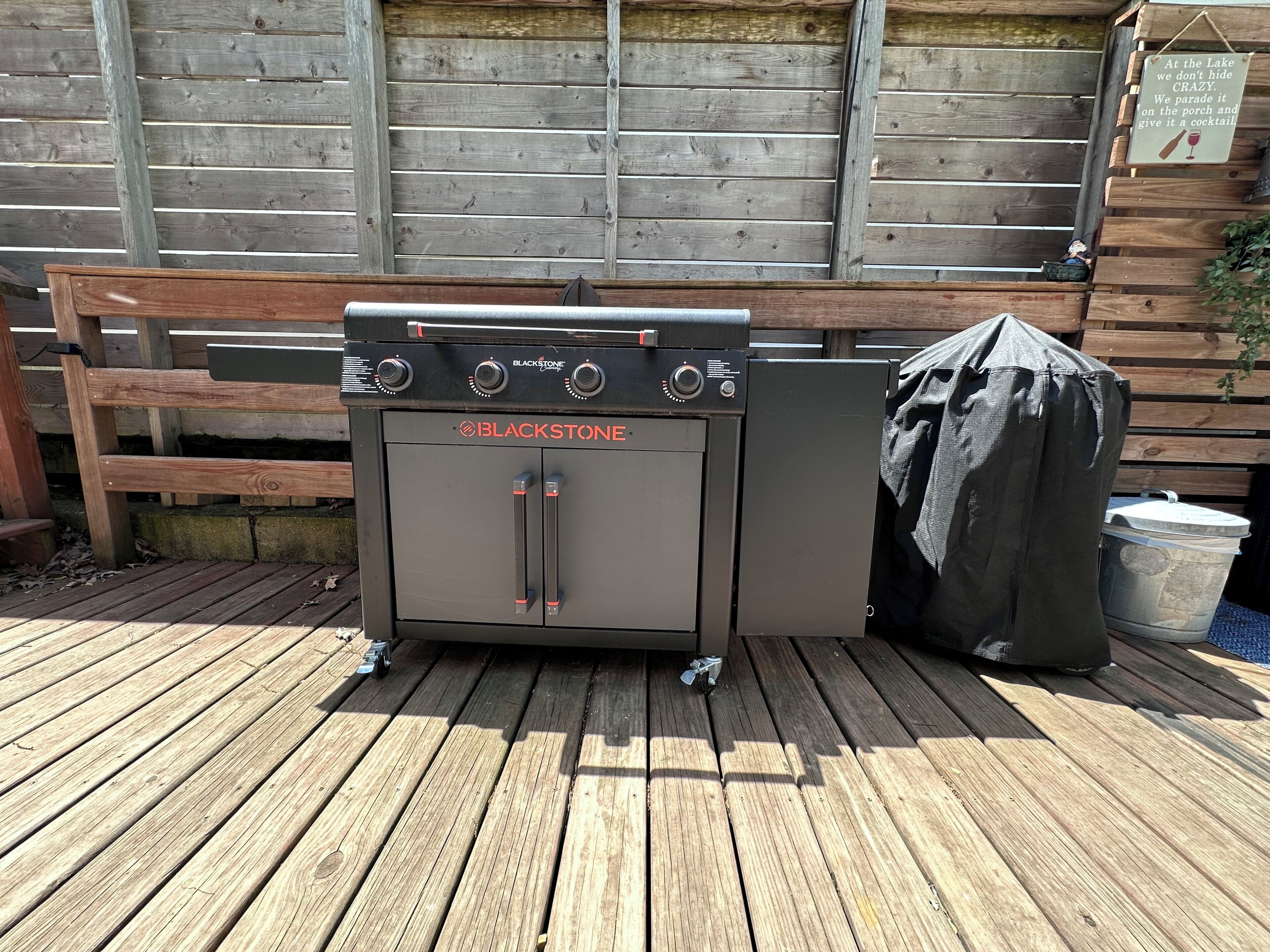 Een BLACKSTONE grill op een houten terras, met een houten omheining en een bord op de achtergrond.