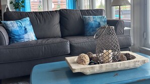 A living room with a grey sofa, blue cushions, a wooden coffee table with decorative items, and a wall with a quote. - Lake-Level Retreat w Hot Tub, Picture Windows & 65” TV for Ultimate Relaxation (Monticello)